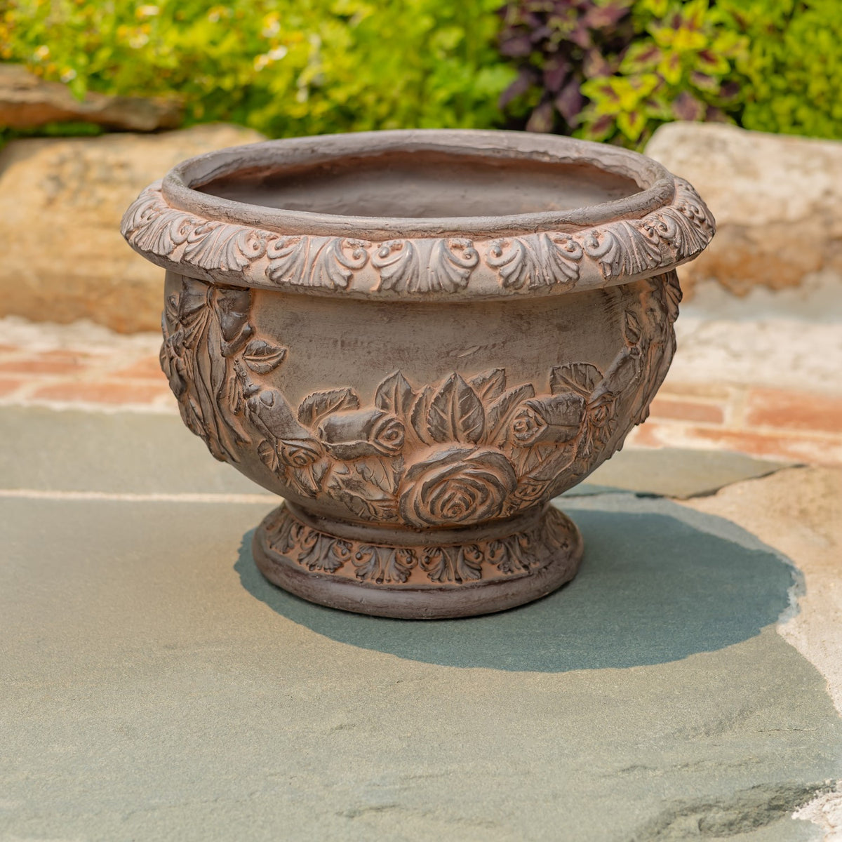 Ornate round planter with raised floral and scrollwork detailing, displayed outdoors on a stone surface.