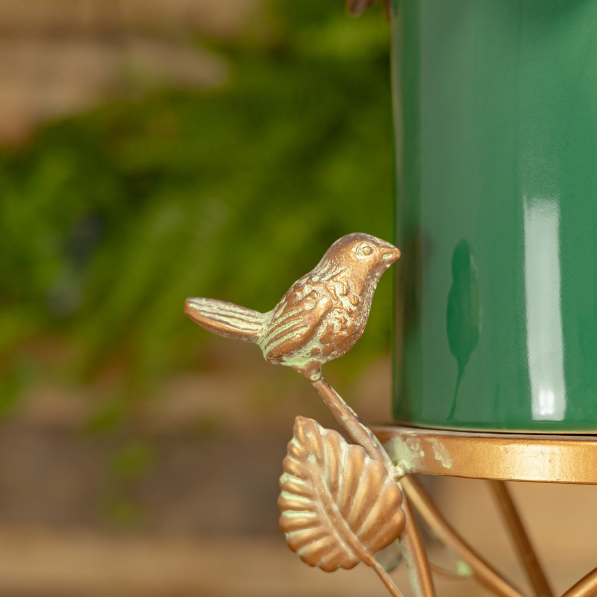 Small textured bird ornament perched beside the glossy green birdhouse body, above a sculpted metal leaf.