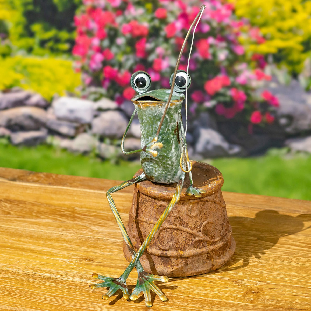 A long-legged metal frog sits on an overturned flowerpot, holding a thin curved wire.