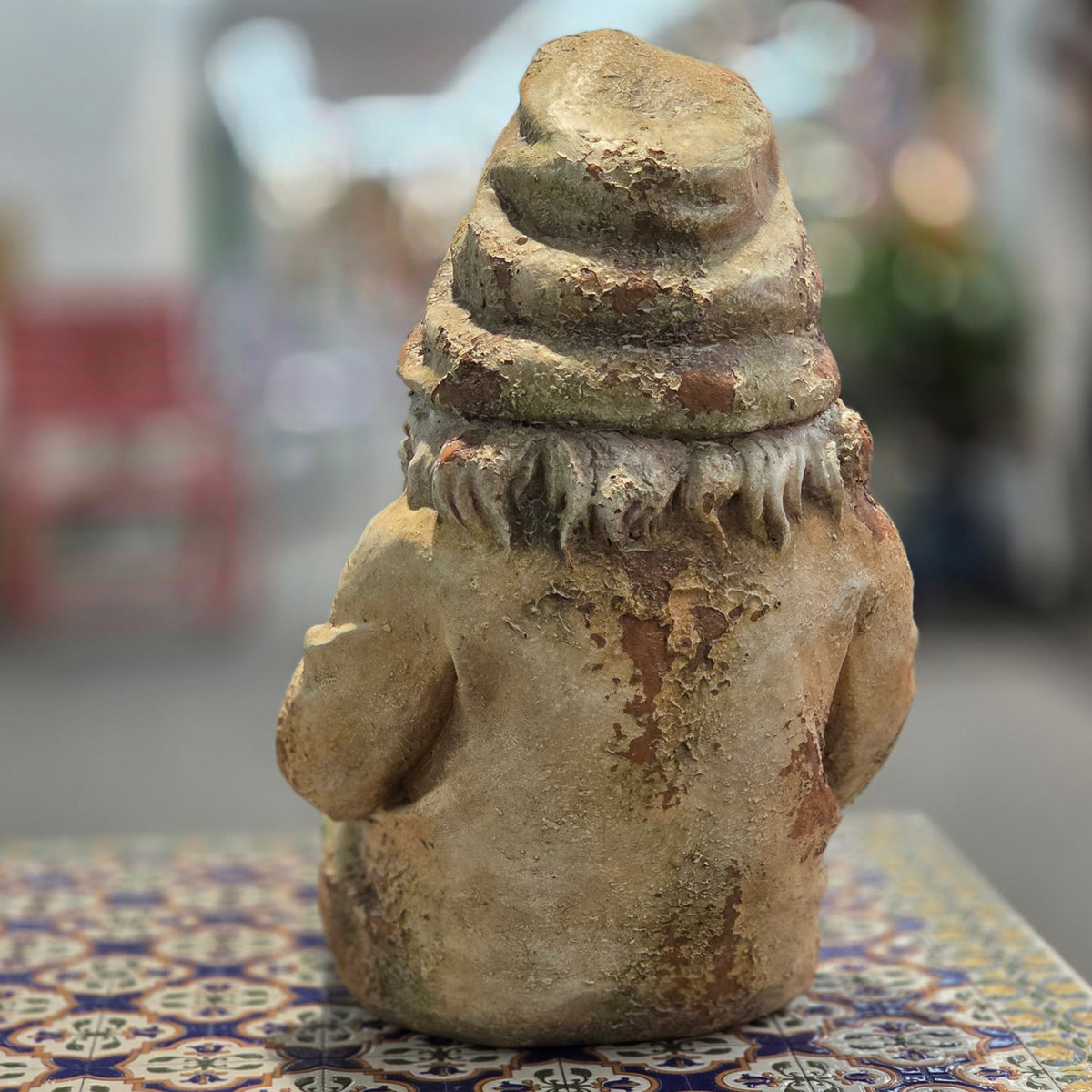 Back view of the distressed garden gnome figurine on a patterned table