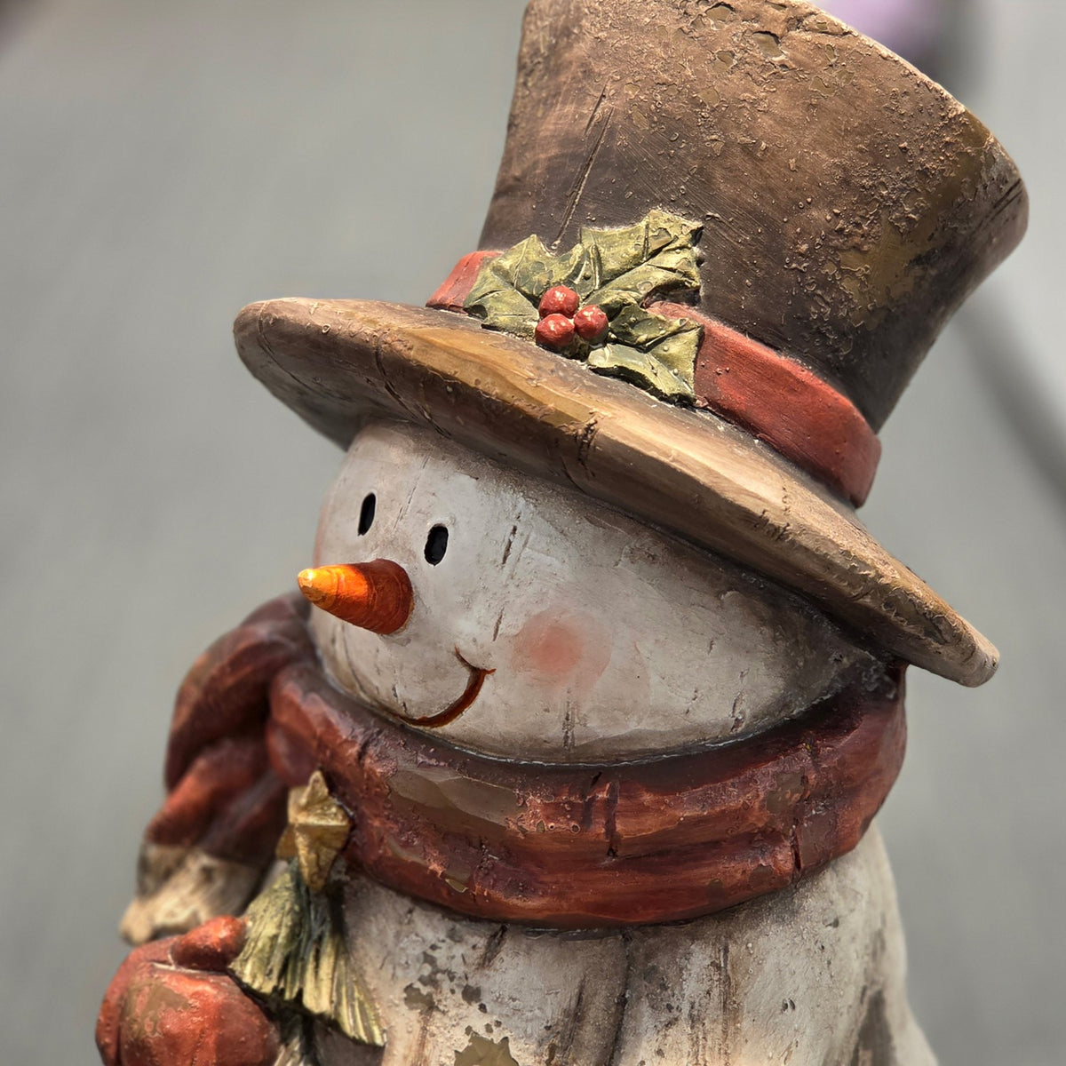 Close-up of snowman figurine's face, scarf, and decorated tree