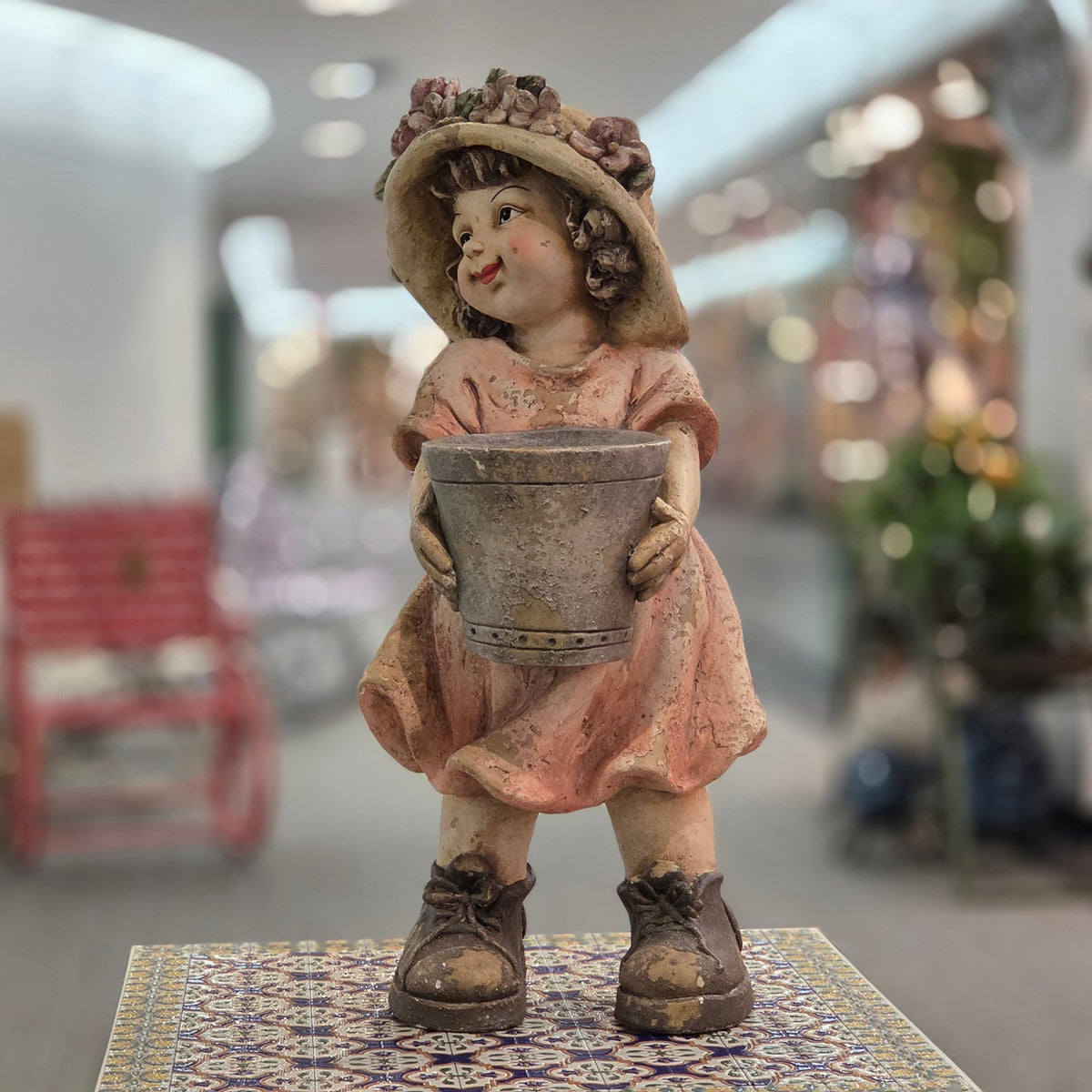 Girl figurine in a pastel dress holding a flowerpot, angled view
