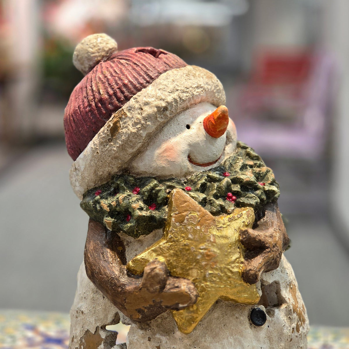 Close view of the snowman's gold star, red hat and textured holly garland