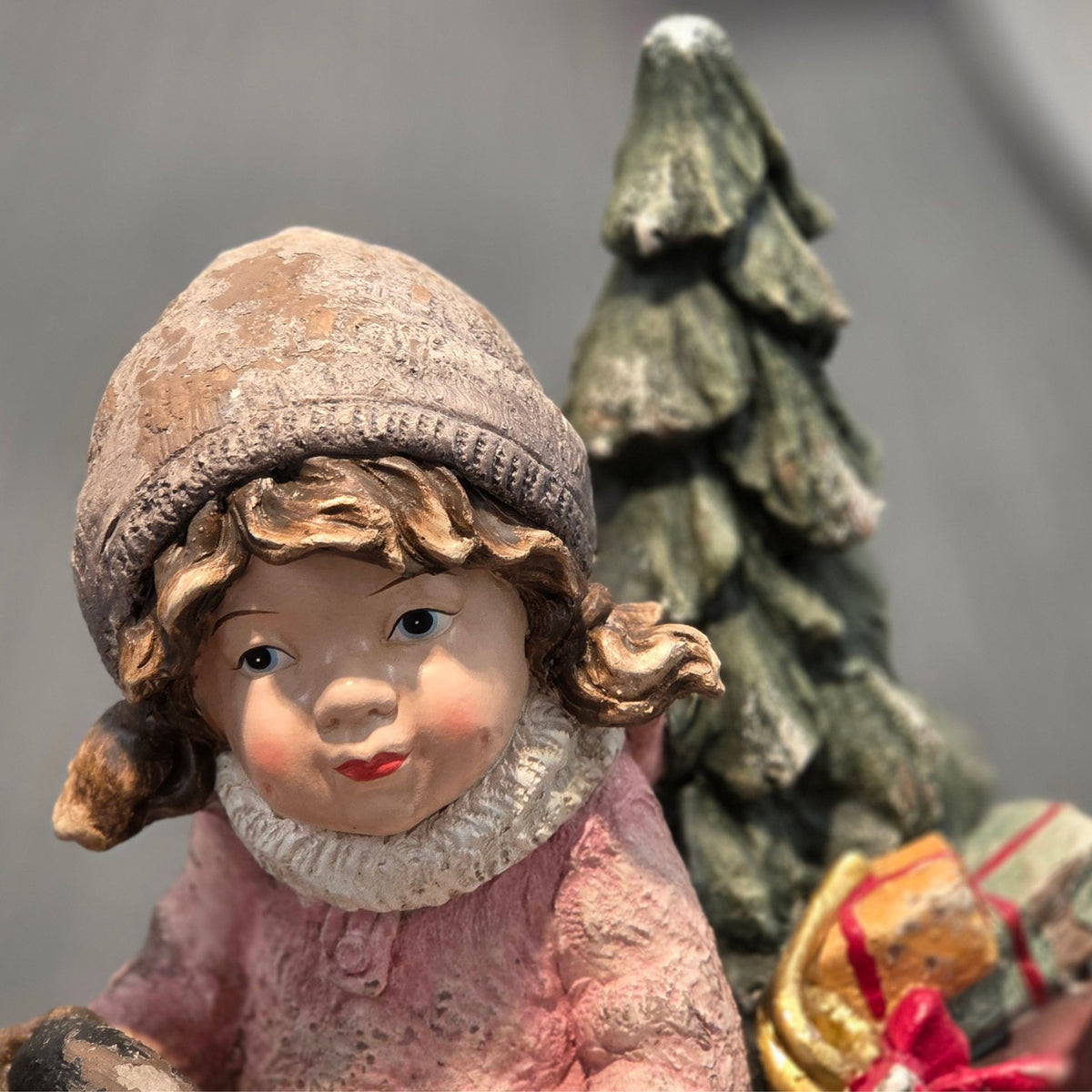 Close-up of the girl's face, knit-style hat, scarf, tree, and gifts