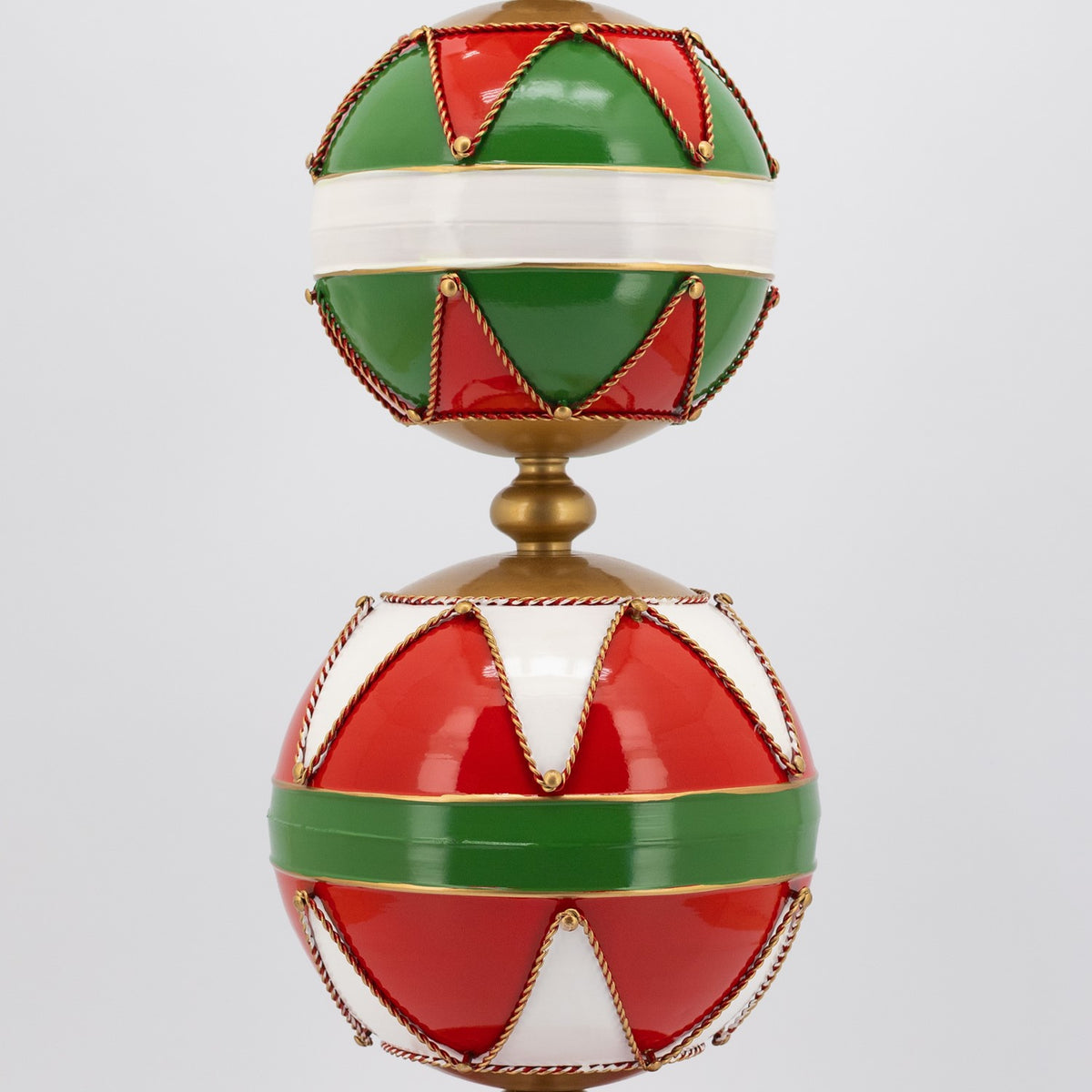 Close-up of two stacked ornaments with alternating red, green, and white panels outlined in gold.