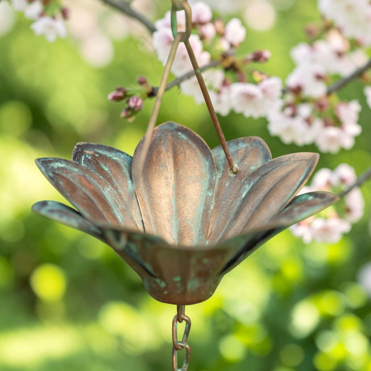 Close-up of a flower-shaped rain chain cup with a weathered copper-colored surface and connecting links.
