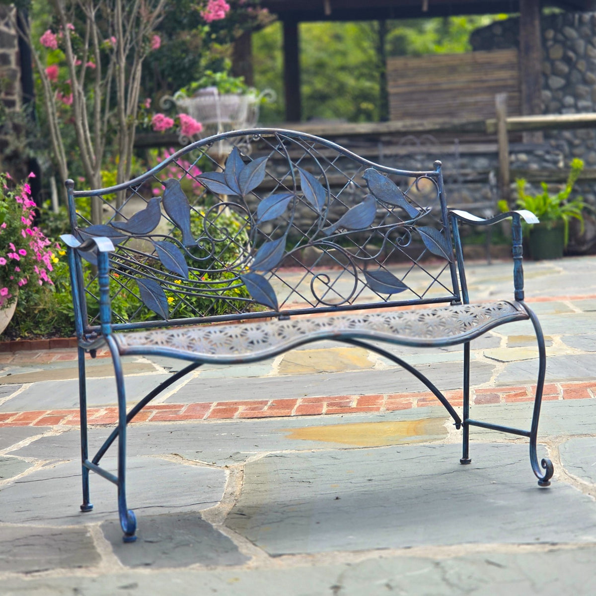 Blue metal bench on a stone path, with leafy backrest ornament and curved armrests visible.