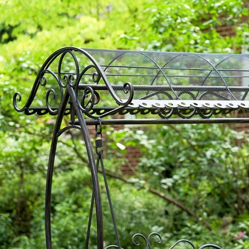 Close view of the curved mesh canopy, scrollwork and hanging frame of a garden swing bench.