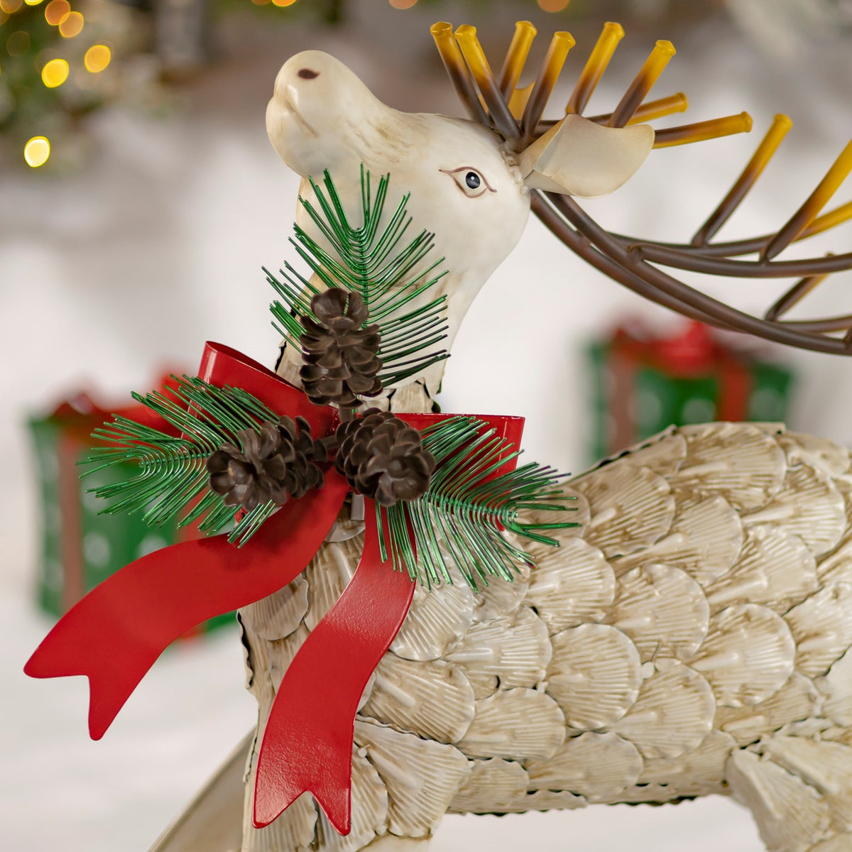 Close-up of a cream reindeer with red bow, greenery and pinecone accents