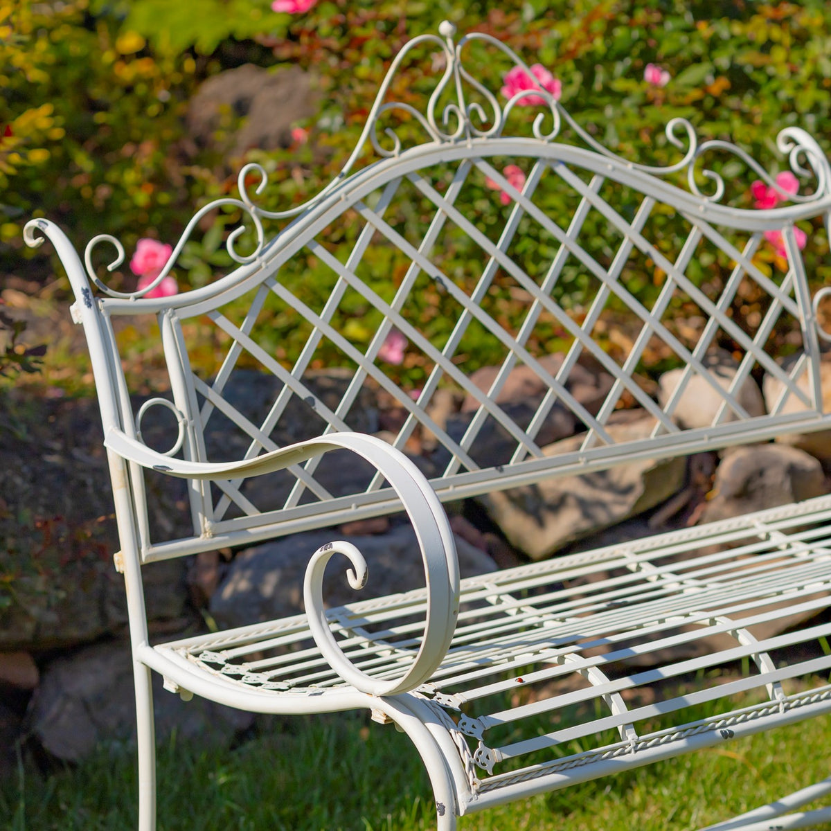 Close-up of the pale iron bench's lattice back, decorative scrollwork and curved arm