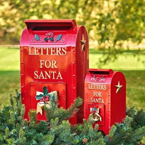 Red Santa mailbox pair with gold accents partly framed by evergreen branches in a garden