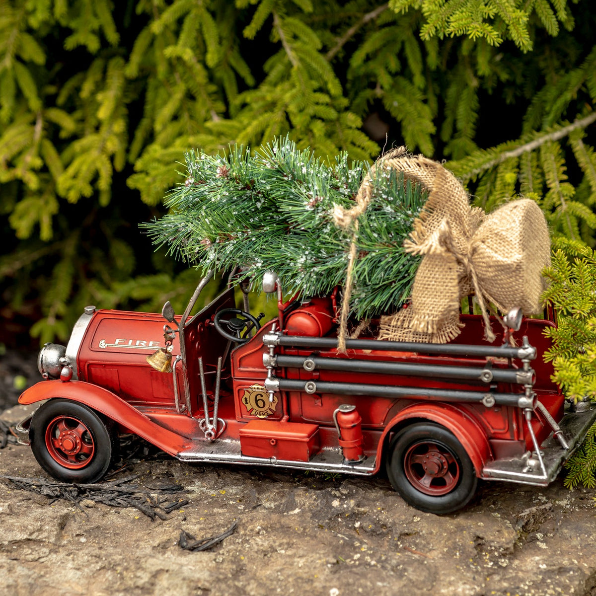 Side view of the red open-cab fire truck carrying an evergreen tree and burlap sack in its rear bed.
