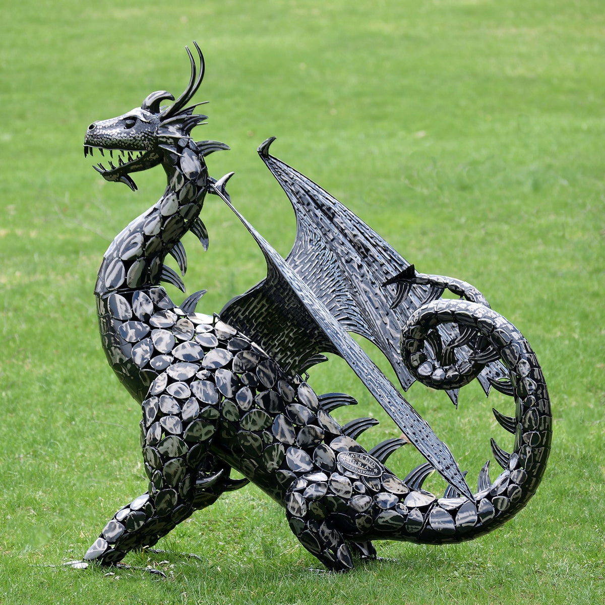 Side view of the metal dragon with overlapping body scales, a large wing, and a looped tail.