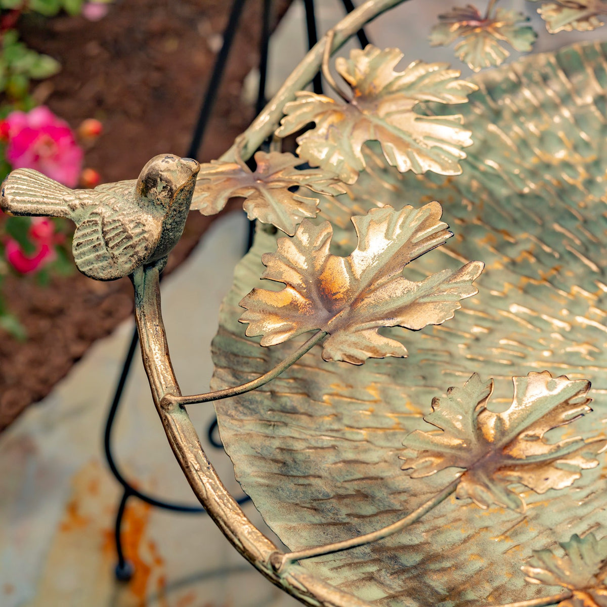 Close-up of a small bird ornament and sculpted leaves attached to the birdbath rim.