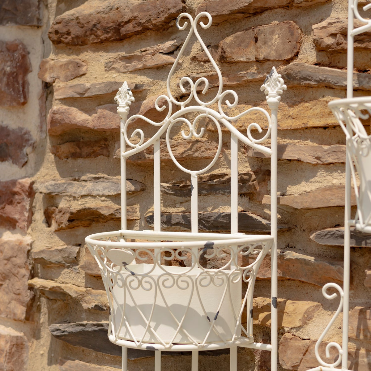 Close-up of the planter’s ornate white metal top and empty basket against a stone wall.