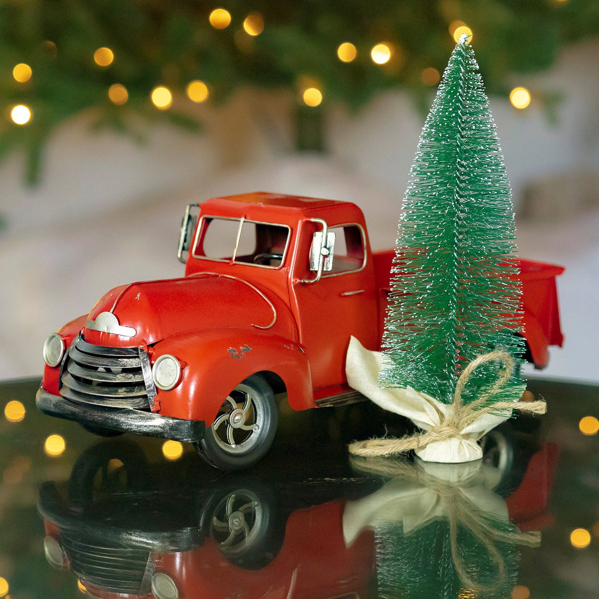 Red vintage pickup beside a separate miniature evergreen tied at its base with twine.