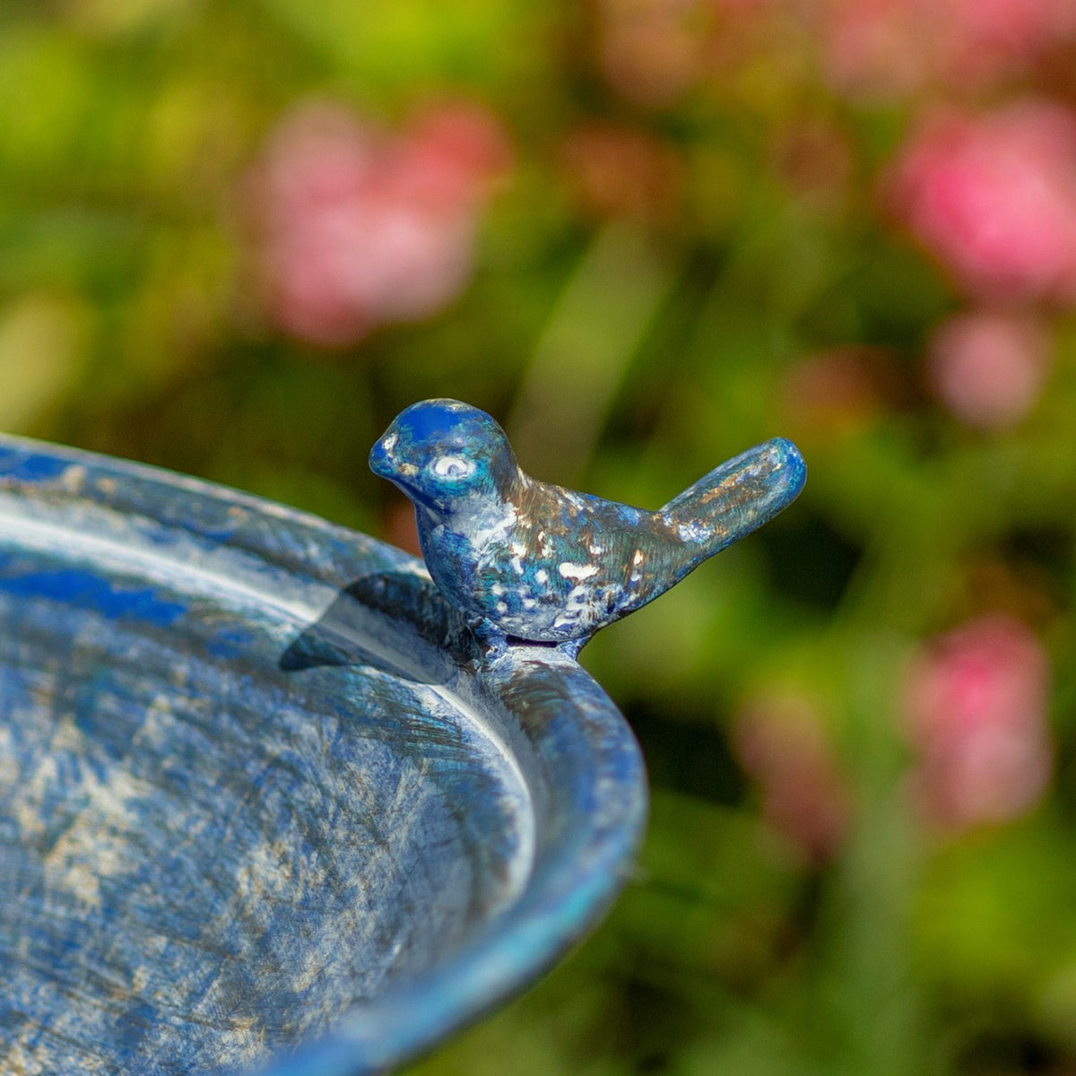 Close-up of a small bird ornament perched on the rim of a mottled blue birdbath.