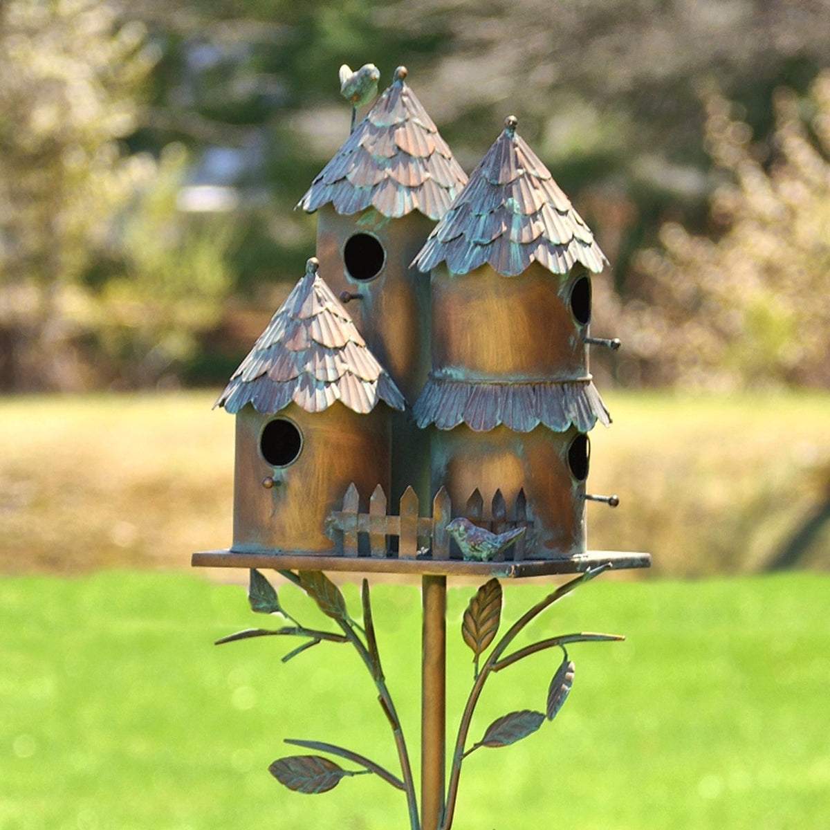 A trio of metal birdhouses tops a slender garden stake with decorative leaves and bird accents.