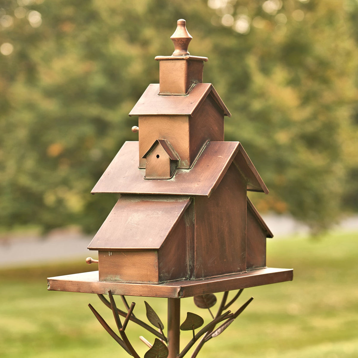 Tall, rust-brown iron birdhouse stake with stacked church-style roofs and decorative branching metal supports, shown