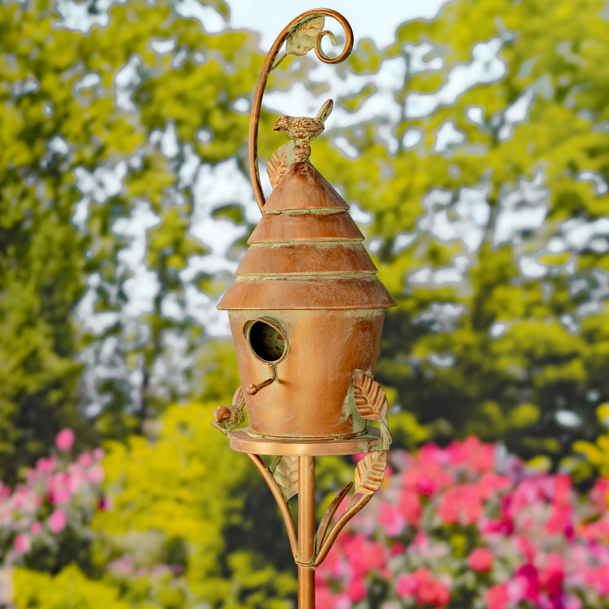Angled view of the birdhouse stake showing its tiered roof, curled top detail and decorative leaves.