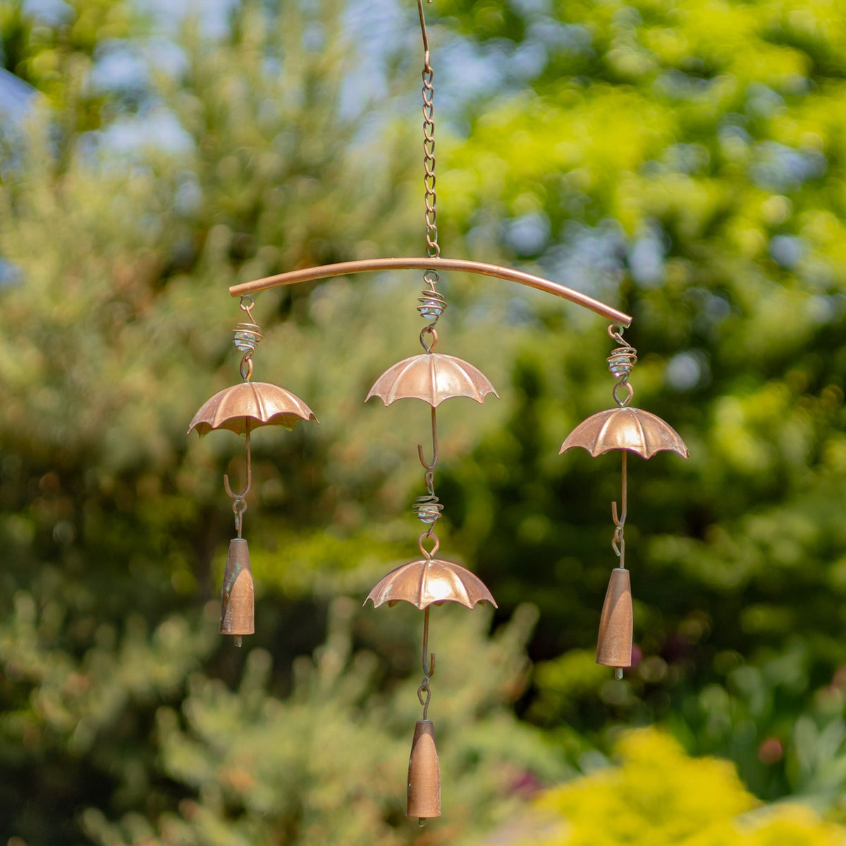 Antique copper umbrella chime hanging from a chain among garden greenery