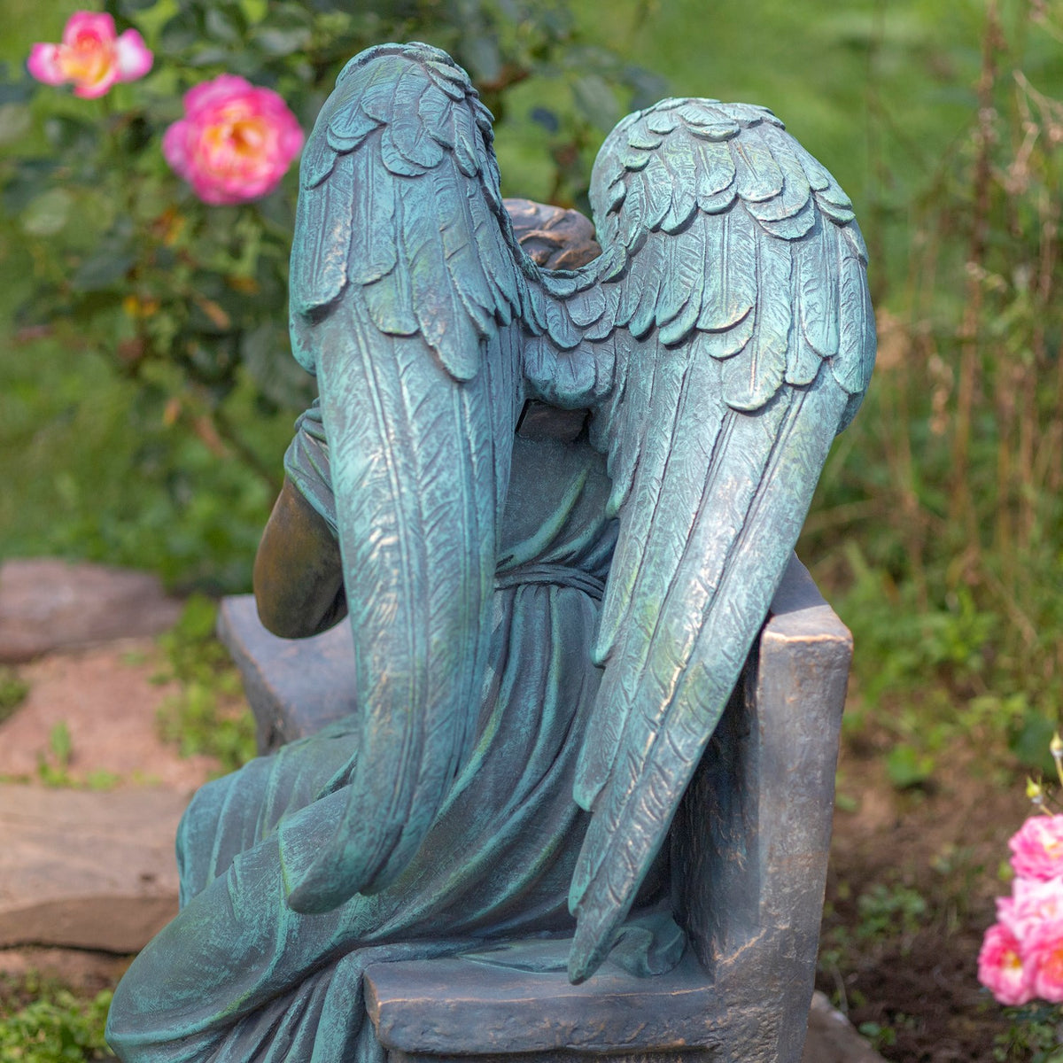 View from behind shows the angel's broad feathered wings and robe against the bench.