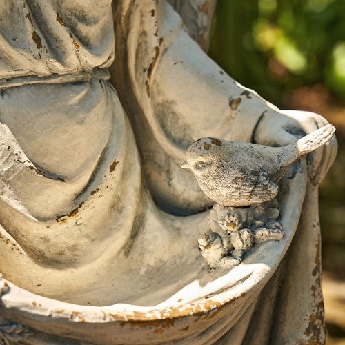 Small bird perched on the edge of the angel statue’s draped garment.