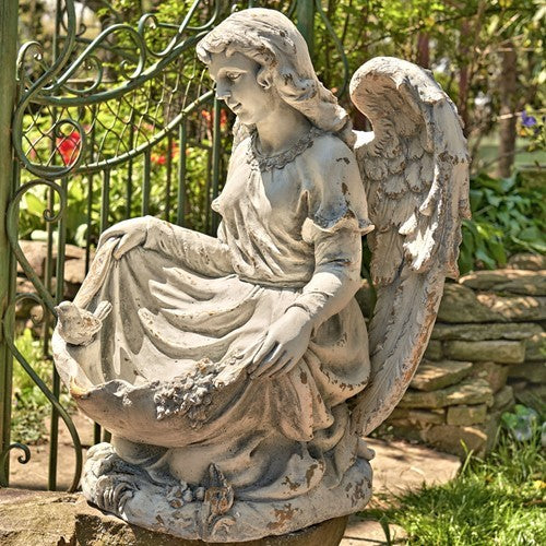 Side view of the seated angel statue, showing its wings, draped robe, and birds.