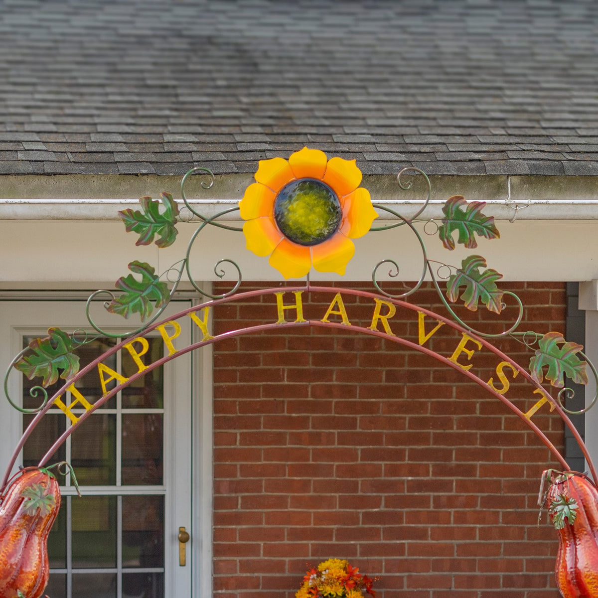 Upper arch detail with a bright sunflower, decorative metal leaves, scrollwork, and curved lettering.