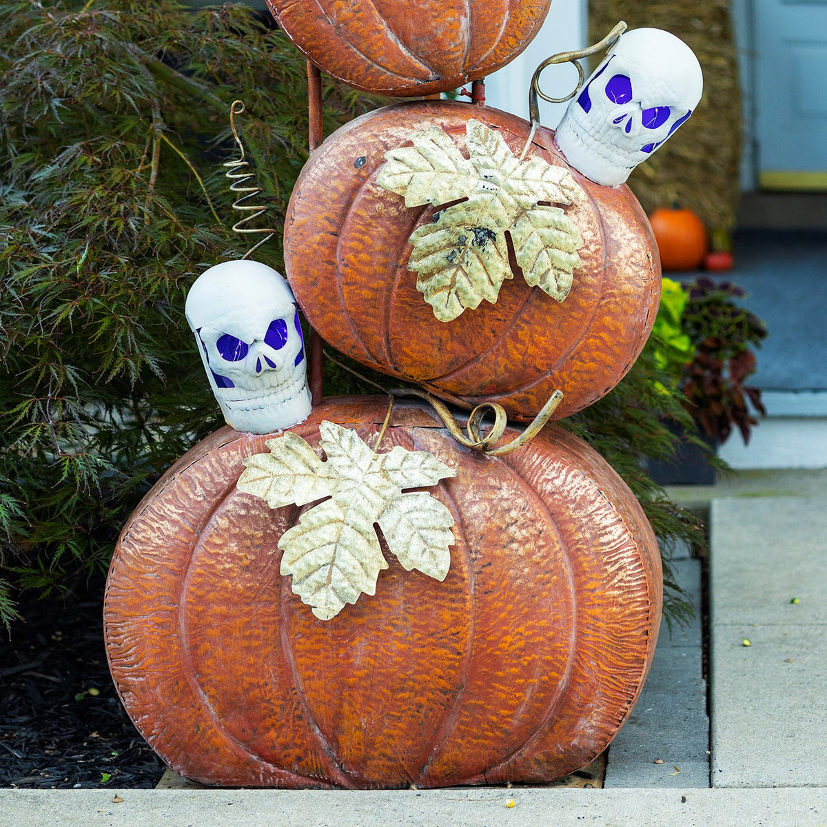 Close-up of large orange pumpkins with pale leaf accents and two white skulls with purple eyes.