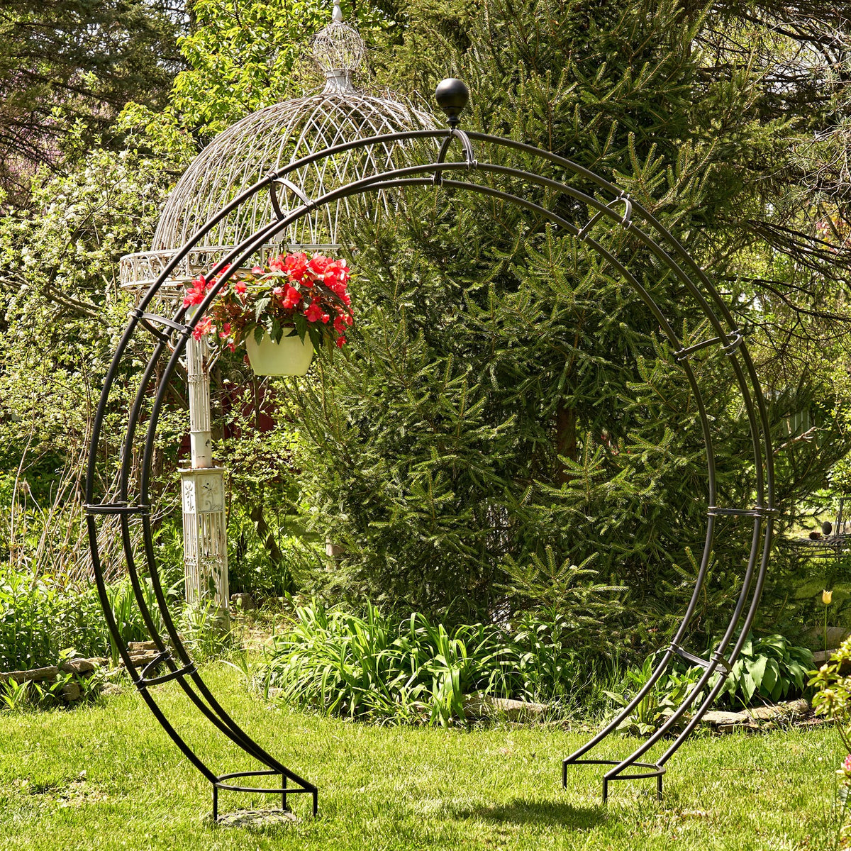 Matte black circular garden arch with a hanging flower basket among greenery