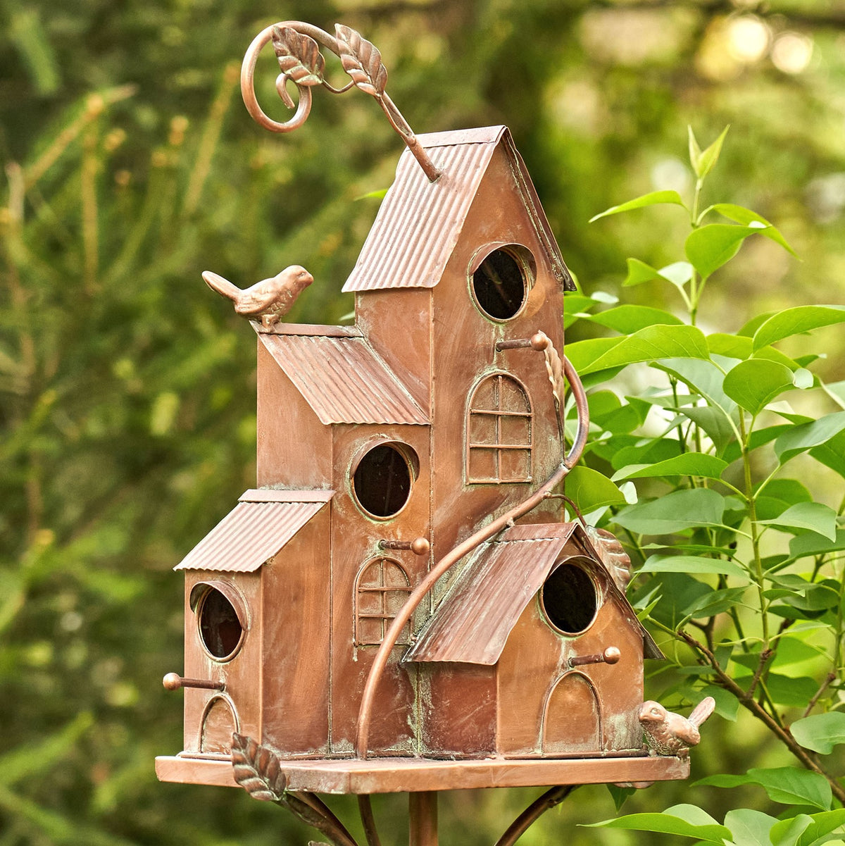 Angled view of the bungalow-style copper birdhouse stake in leafy garden greenery