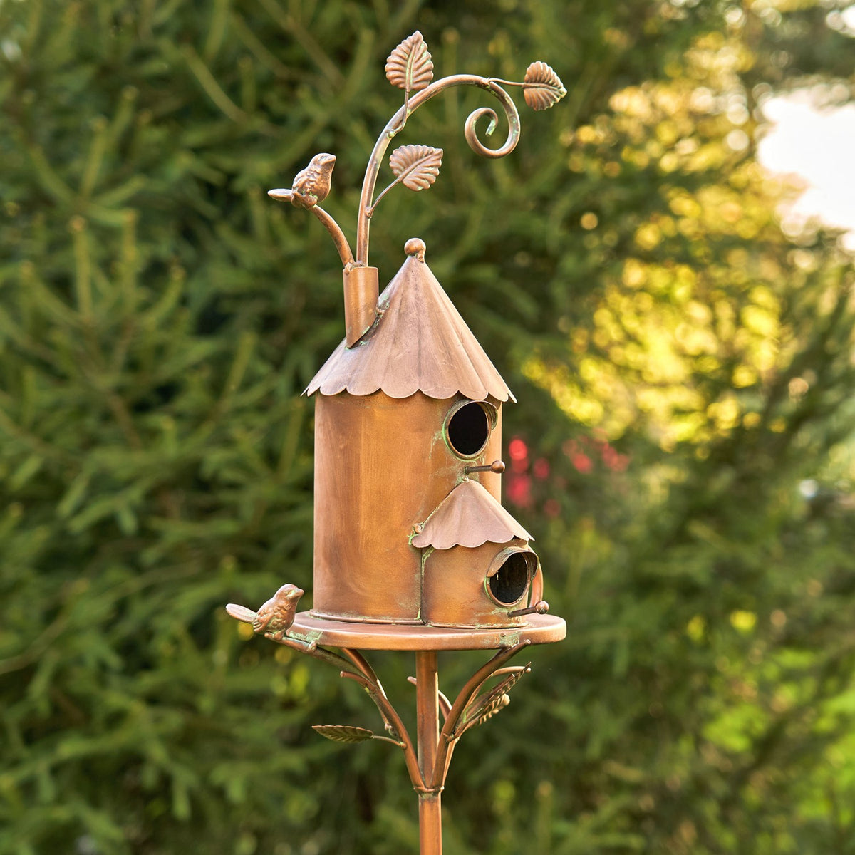 Full view of the antique copper birdhouse and long stake against leafy garden greenery