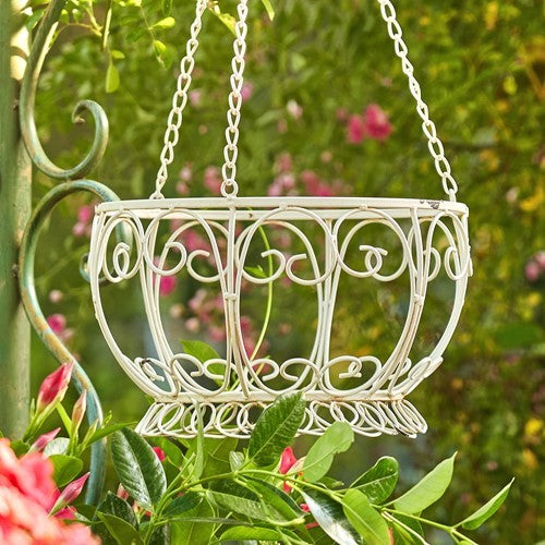 Cream scrollwork hanging basket suspended among green leaves and pink flowers