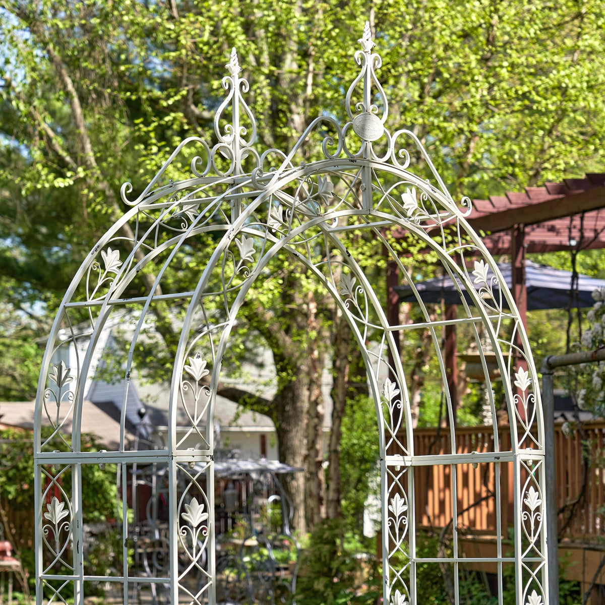 Close view of a pale metal garden arch with ornate scrollwork and floral accents.