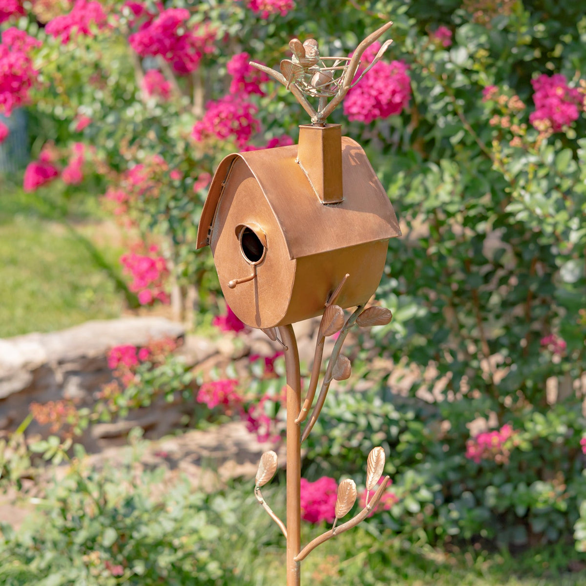 Angled view of the birdhouse showing its round entrance, curved roof, decorative leaves, and slender stake.