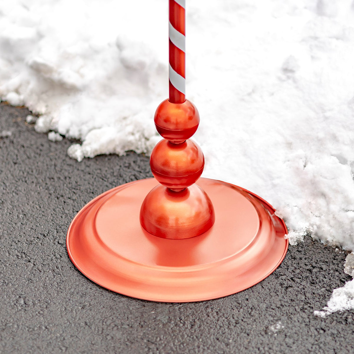 Close-up of the lantern’s round red base and stacked spherical accents on snowy pavement.