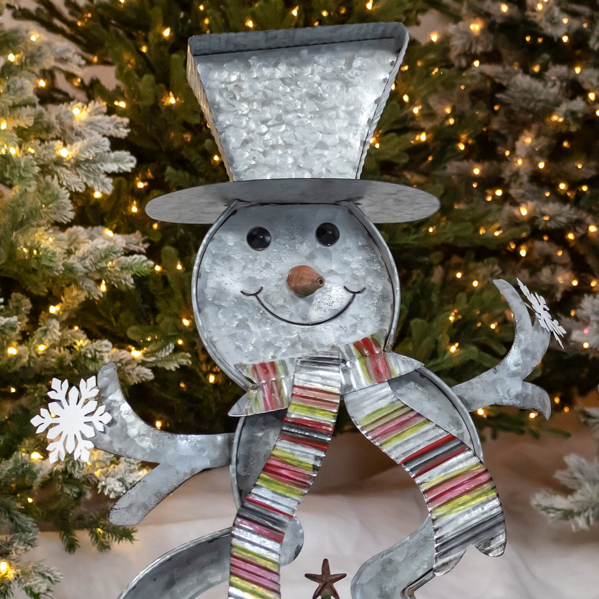 Close-up of a galvanized snowman’s smiling face, tall hat, striped scarf and outstretched arms.