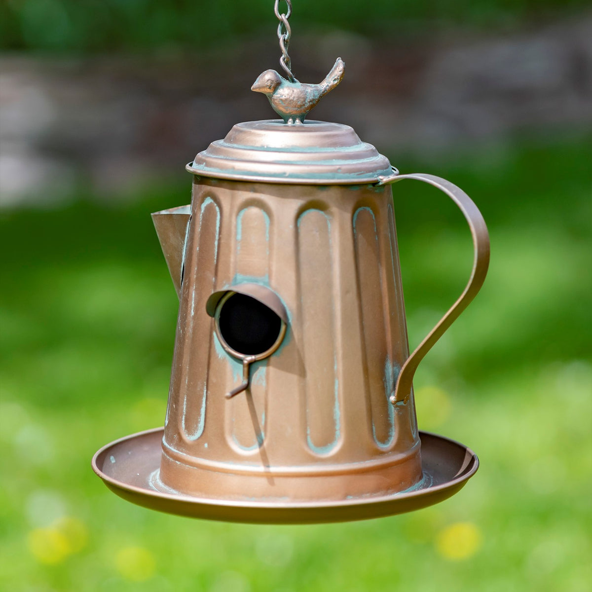 Fluted teapot-shaped birdhouse with a curved handle, circular entrance, hanging chain, and bird ornament on top.