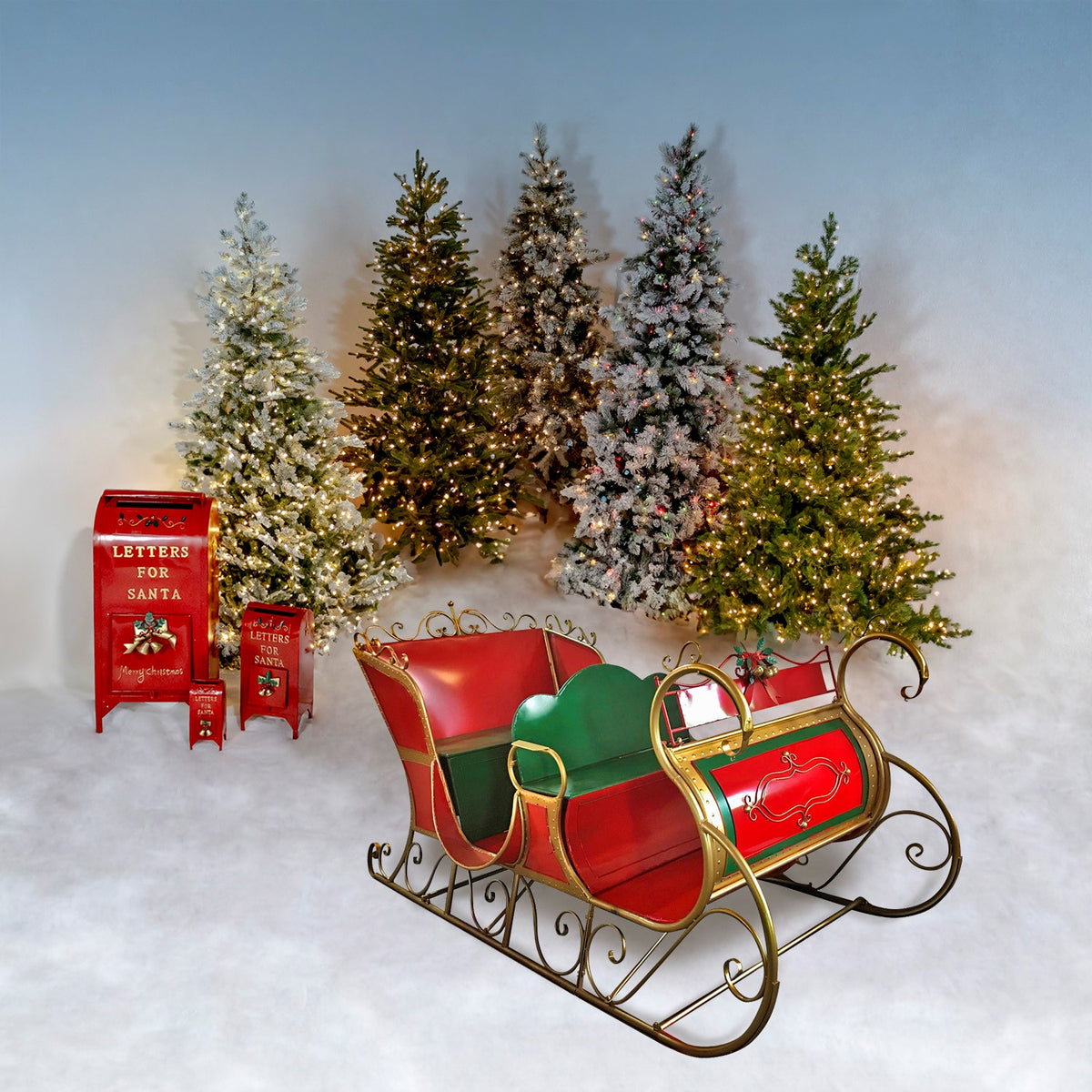 Red and green decorative sleigh displayed with Christmas trees on a pale backdrop