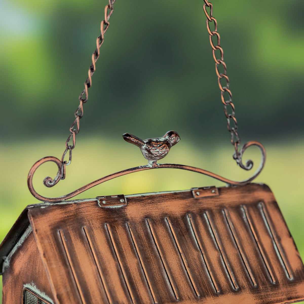 A small bird ornament sits above the ridged roof between curled metal supports and hanging chains.