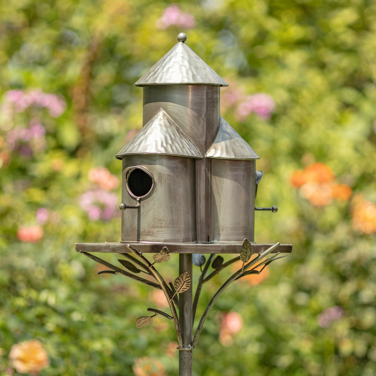Side angle of the silver triple birdhouse stake, showing overlapping roofs and its leaf-decorated platform support.