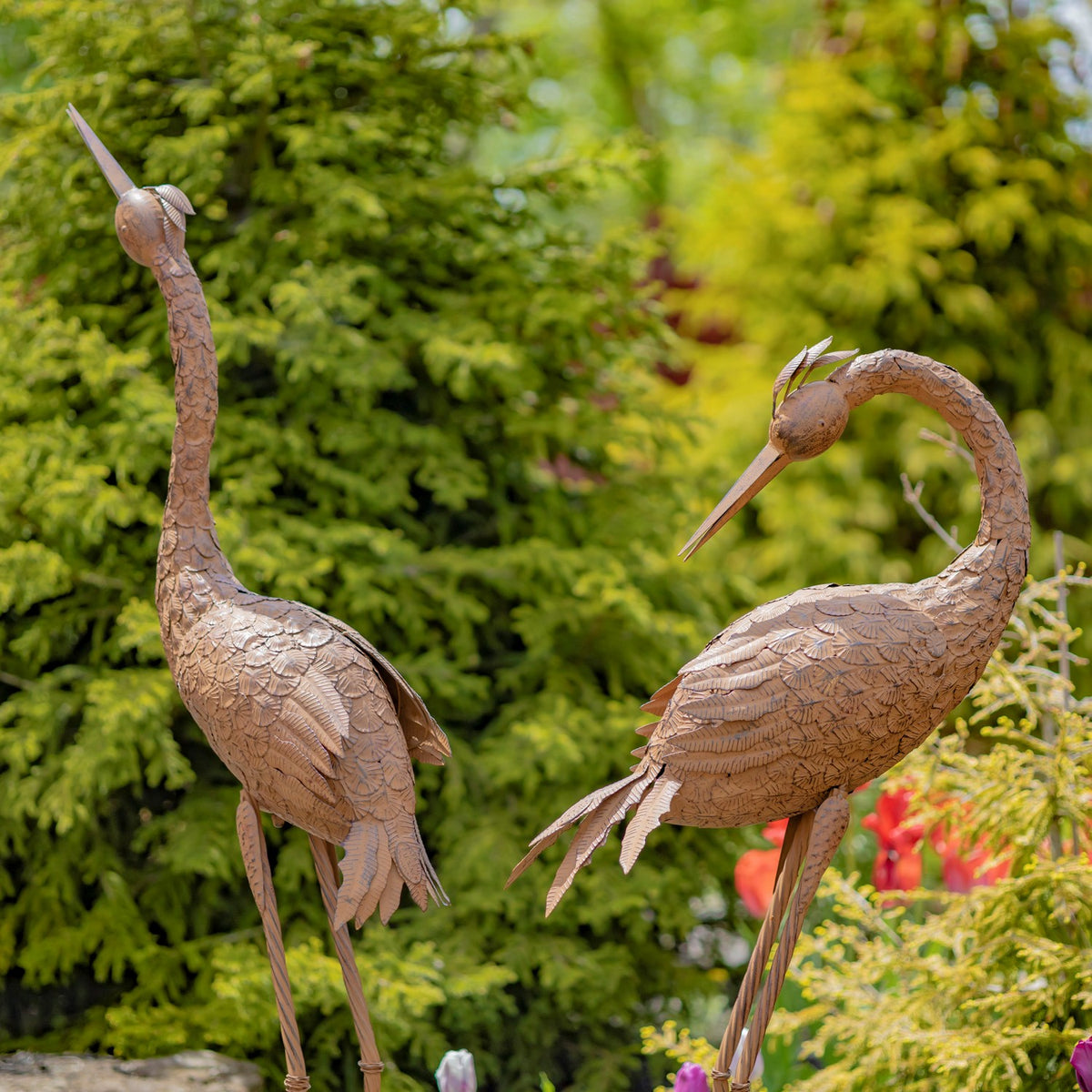 Rear and side view of two rust-colored crane sculptures among flowers