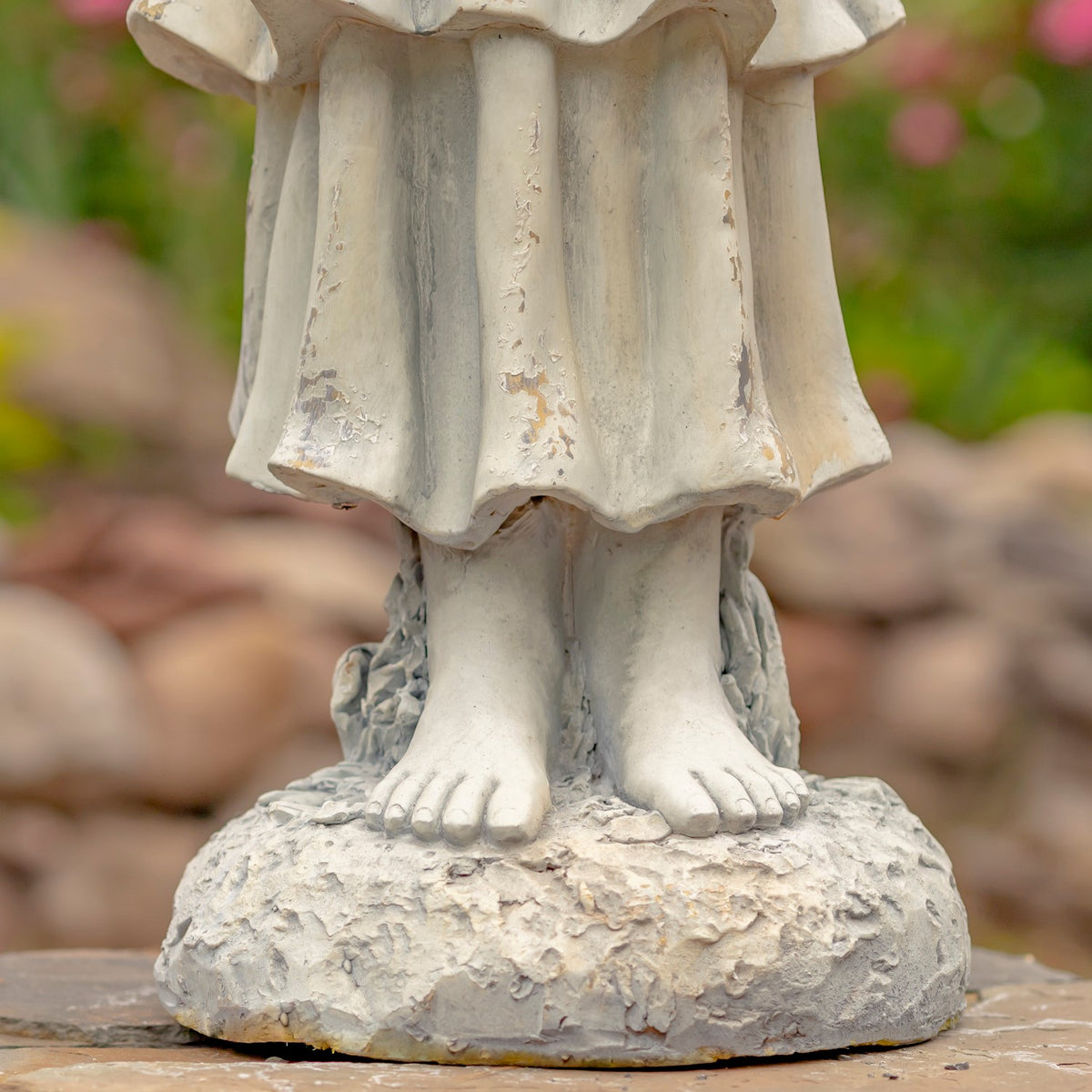 Close view of the angel statue’s weathered robe, bare feet and textured round base.