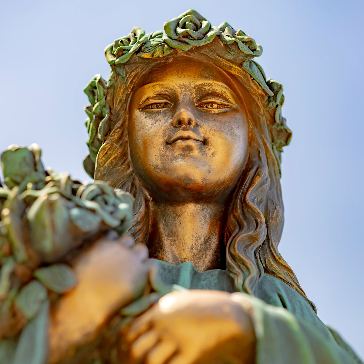 Low-angle close-up of the statue’s face and rose crown against a clear sky.
