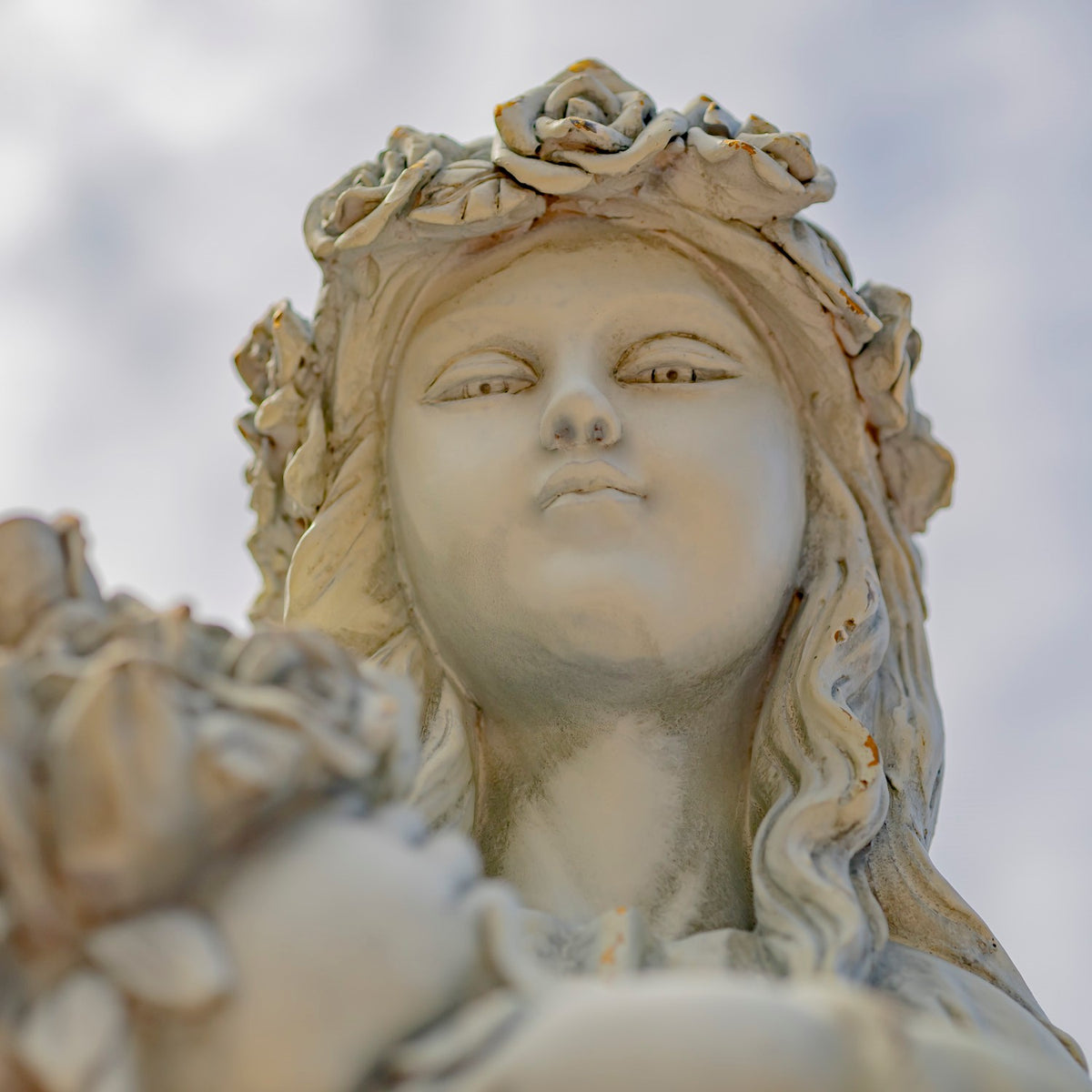 Close-up of the angel’s serene face and rose crown against the sky.