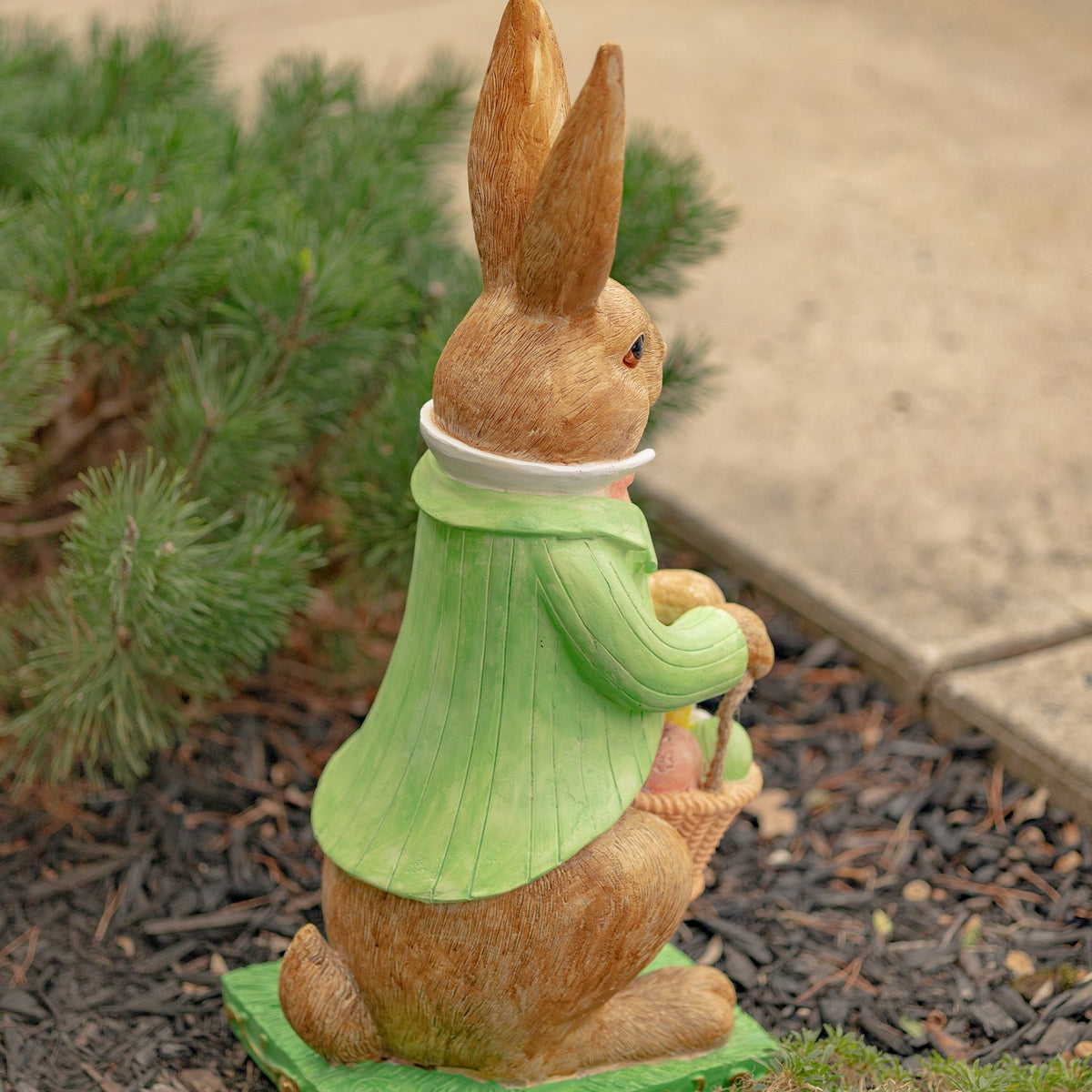 Rear view shows the rabbit statue’s green jacket, seated pose, and basket at its side.
