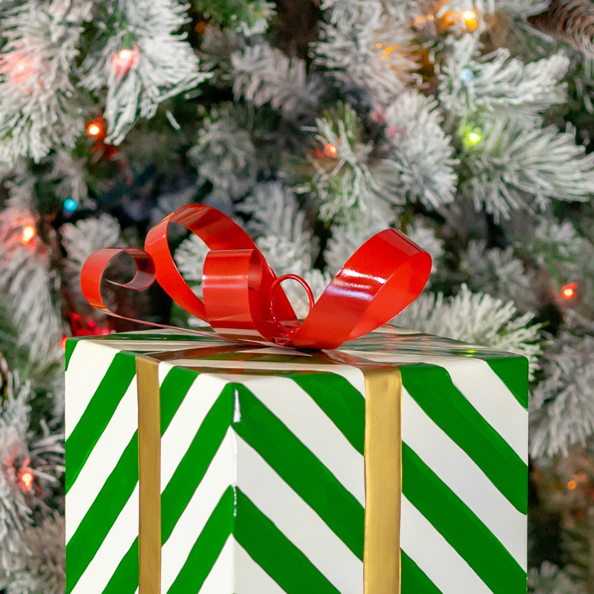 Upper portion of the striped gift box with a glossy red bow against snowy tree branches.