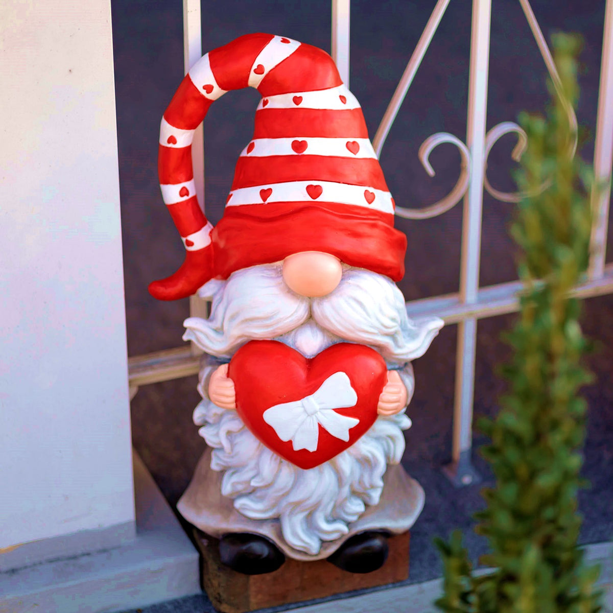 Front view of a heart-holding Valentine gnome beside a porch railing