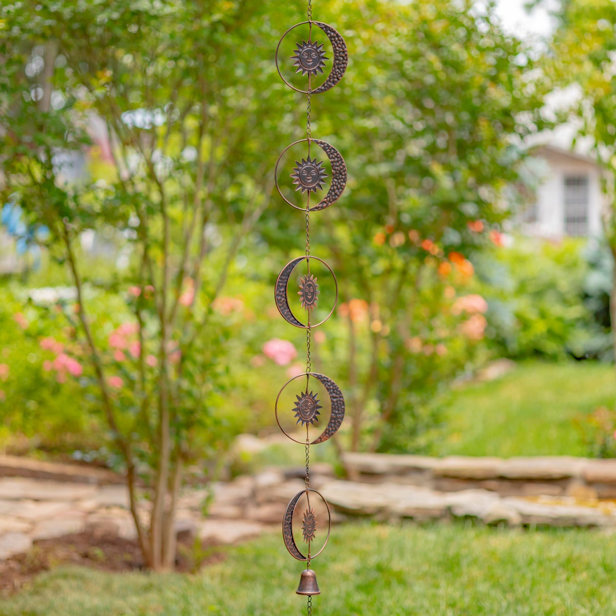 Full rain chain with repeated sun and crescent moon pieces in a garden setting